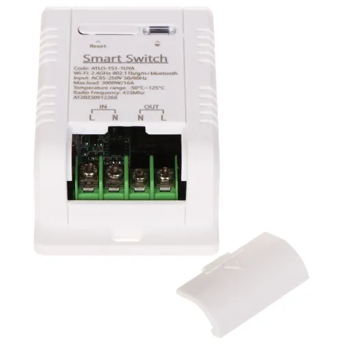 Zdjęcie przedstawia biały inteligentny przełącznik z widocznymi złączami i oznaczeniami technicznymi na obudowie. Obok urządzenia leży zdjęta pokrywa, ukazując wnętrze z zielonymi terminalami.