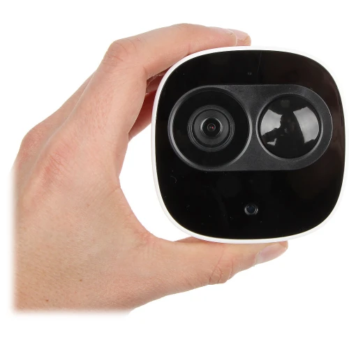 Na zdjęciu znajduje się kompaktowa kamera monitorująca w białej obudowie, trzymana w dłoni. Kamera ma czarny panel przedni z widocznym obiektywem i czujnikiem.