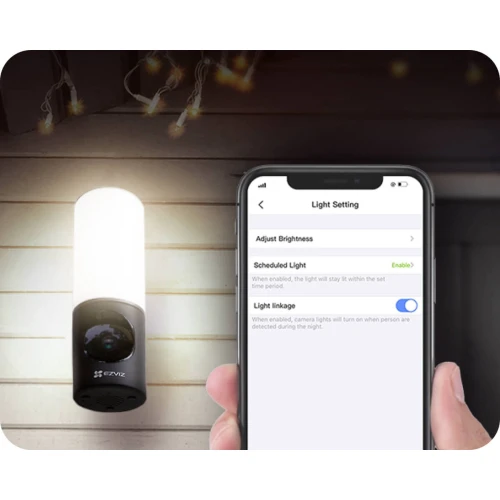 Bezprzewodowa kamera WiFi 4MP zintegrowana z lampą, zamontowana na zewnętrznej ścianie budynku, oferuje funkcję regulacji jasności światła przez aplikację na smartfonie. Urządzenie zapewnia monitoring i oświetlenie, co zwiększa bezpieczeństwo posesji.