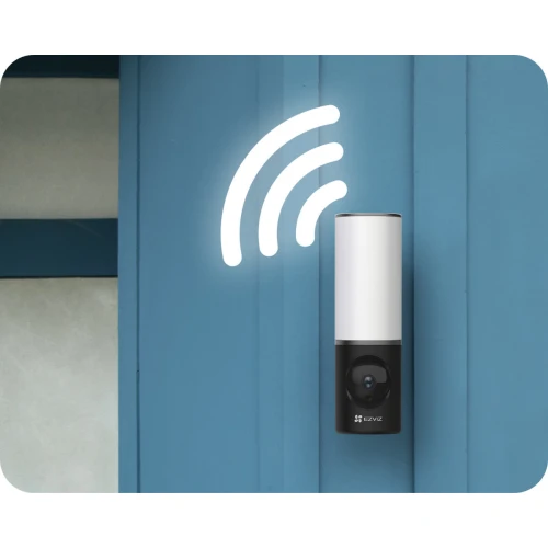 Bezprzewodowa kamera WiFi 4MP marki EZVIZ zamontowana na niebieskiej ścianie, z widocznym symbolem sygnału bezprzewodowego. Urządzenie ma nowoczesny, cylindryczny kształt z białą górną częścią i czarną dolną, w której znajduje się obiektyw.