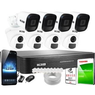 Na zdjęciu znajduje się zestaw do monitoringu, w skład którego wchodzą cztery kamery, rejestrator, dysk twardy Toshiba oraz akcesoria takie jak myszka i przewody. Obok zestawu widoczny jest również znak informujący o monitorowaniu obiektu.