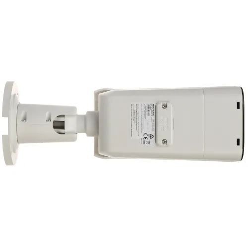 Zdjęcie przedstawia biały, prostokątny aparat monitoringu zamontowany na uchwycie ściennym, widziany od spodu. Na obudowie widoczne są etykiety z informacjami technicznymi i certyfikatami.