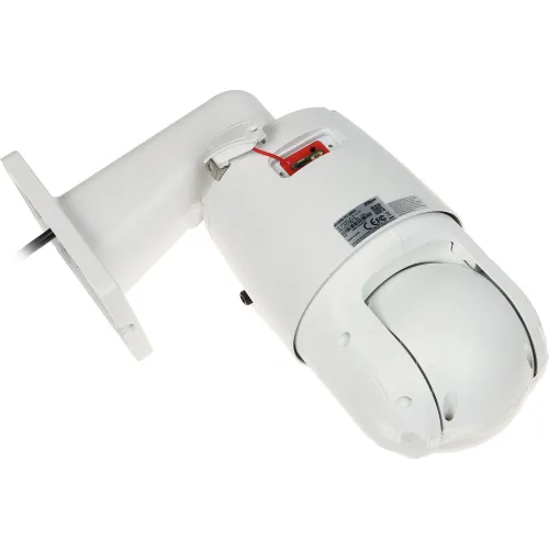 Na zdjęciu znajduje się biała kamera monitoringu zamontowana na ściennym uchwycie, z widocznymi przewodami i etykietą techniczną. Kamera ma kulisty kształt i jest skierowana w dół.