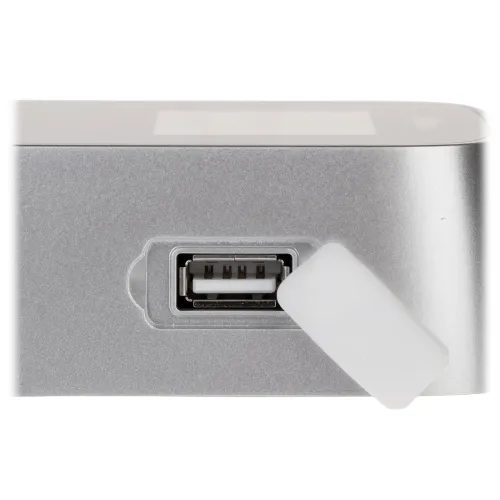 Zdjęcie przedstawia zbliżenie na srebrne urządzenie z widocznym portem USB, osłoniętym białą zaślepką. Port znajduje się na bocznej powierzchni urządzenia, które ma gładkie, metaliczne wykończenie.